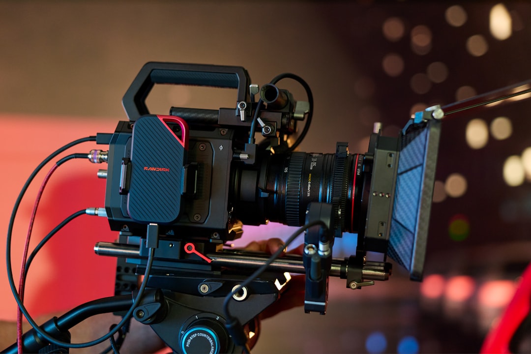 A professional video camera on a tripod with blurred lights.